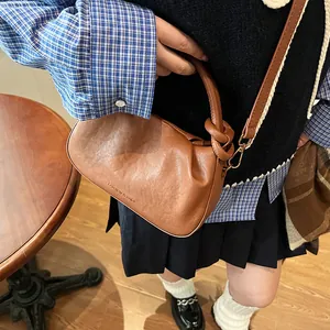 Close-up of pleated brown leather bag with knotted handle and fashion text detail