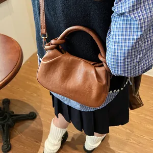 Brown pleated cloud bag with round handle and adjustable strap shown in cafe setting