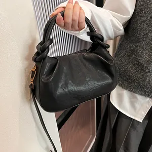Detail of black pleated cloud bag with knotted handle and golden metal hardware