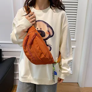 Detail der orangefarbenen Canvas-Brusttasche mit Stickerei und grünem Karabiner-Anhänger