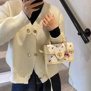 Dettaglio della borsa a mano color crema con stampa ciliegia, chiusura dorata e charm a ciliegia