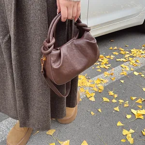 Detail of soft brown pleated cloud bag with knotted handle and golden buckle in autumn setting