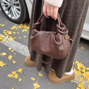 Detailed close-up of dark brown wrinkled leather bag with unique knotted handle and gold hooks
