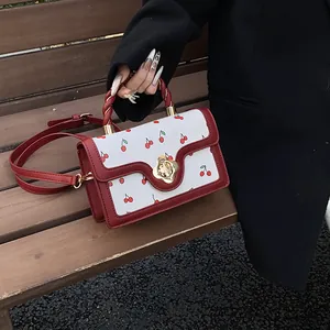 Dettaglio di una borsa bianca con stampa ciliegia e bordo rosso su panca di legno
