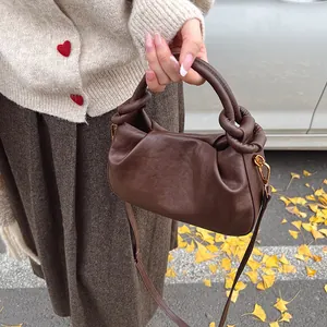 Detail of a dark brown pleated cloud bag featuring a knotted handle and gold metal hardware
