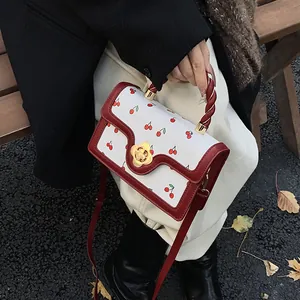 Dettaglio manico intrecciato rosso e chiusura a fiore dorata su borsa con ciliegie