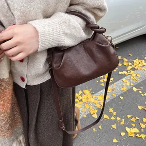 Detail of dark brown ruched cloud bag with knotted handle on autumn ginkgo leaves