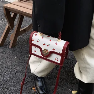 Dettaglio borsa bianca con stampa ciliegie, chiusura a fiore dorato e tracolla rossa