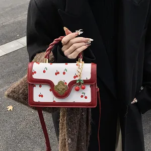 Dettaglio borsa con stampa ciliegia con chiusura a fiore dorato e manico a treccia rosso