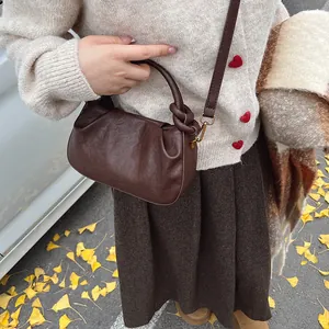 Detail of dark brown ruched cloud bag with knotted handle and elegant gold hardware