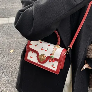 Scatto in strada di una borsa a tracolla bianca con stampa ciliegie, manico rosso e fibbia