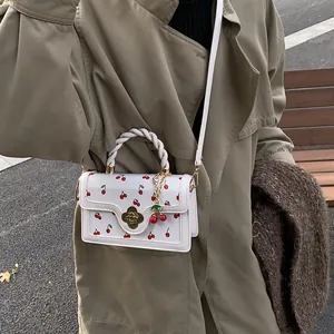 Dettaglio di una borsa a tracolla bianca con stampa ciliegia abbinata a un trench kaki