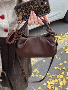 Deep brown ruched cloud bag with knotted handle and shoulder strap in outdoor scene