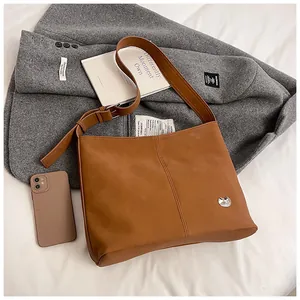 Detail of vintage brown tote bag with metal owl logo and adjustable wide strap on a coat