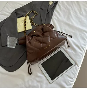 Detail of coffee quilted bucket bag featuring a gold chain strap and soft pleated texture