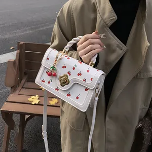 Dettaglio borsa in pelle bianca con stampa ciliegie e chiusura a fiore dorato
