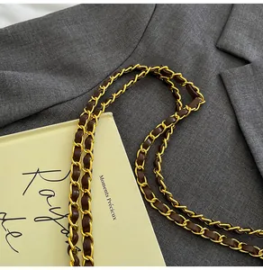 Detail of the golden metal chain interlaced with dark brown leather on a shoulder bag