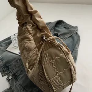 Detail of light khaki quilted bag with wave stitching and ruched strap on denim jacket