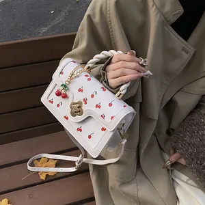 Dettaglio borsa bianca con stampa ciliegia, chiusura floreale e manico intrecciato su modella