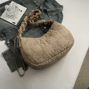 Close-up of beige quilted crossbody bag featuring wave stitching and ruffled shoulder strap