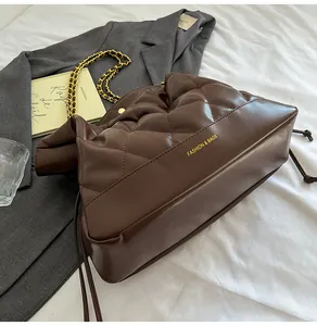 Detail of coffee quilted bucket bag with gold chain strap on a white bedding backdrop