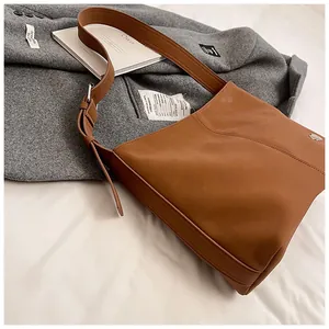 Detail of a brown matte leather tote bag with wide adjustable strap and metal buckle