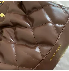 Close-up of dark brown quilted leather texture and golden fashion logo on a bucket bag