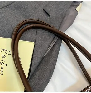 Detail of round dark brown leather handles with fine stitching on a tote bag