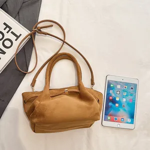 Detail of a brown suede tote bag with golden metal buckle on a white fabric background