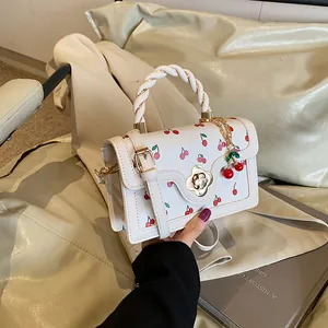 Dettaglio della borsa bianca con stampa ciliegie, manico intrecciato e chiusura floreale