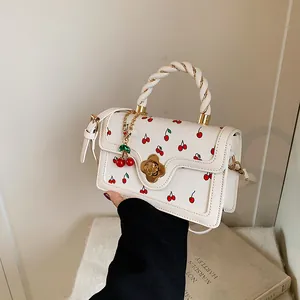 Dettaglio della borsa in pelle bianca con stampa ciliegia, fibbia a fiore e manico