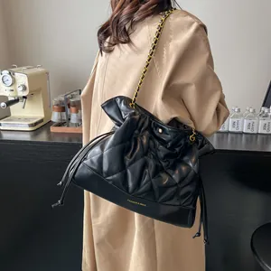 Detail of black quilted leather shoulder bag with gold chain strap on beige trench coat