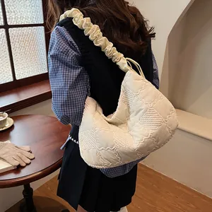 Detail of cream quilted crossbody bag featuring a ruched strap and diamond texture