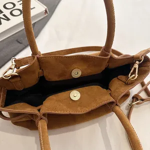 Detail of caramel suede tote bag with magnetic buckles and sleek golden hardware