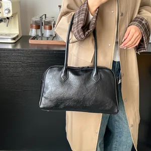 Detail of black glossy tote bag with pleated leather texture worn by a model in a cafe