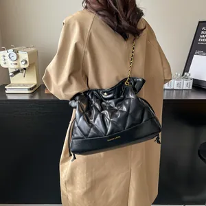 Detail of black quilted leather bucket bag with gold chain and drawstring closure