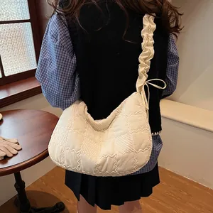 Close-up of white quilted dumpling bag with ruffled strap and bow details on a model