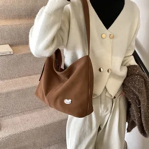 Detail of a large brown tote bag with a unique silver metal buckle and matte texture