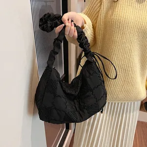 Detail of black quilted puffer bag featuring gathered handles and decorative side bows