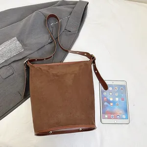 Detailed close-up of brown suede bucket bag with adjustable gold buckle shoulder strap