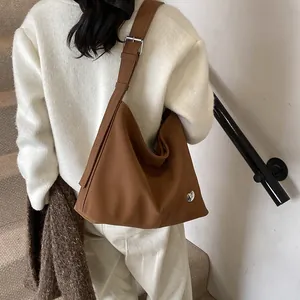 Close-up of brown leather tote bag featuring a silver heart charm and adjustable strap