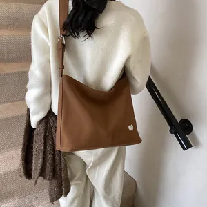 Detail of a brown leather tote bag with silver heart logo on a soft matte finish surface