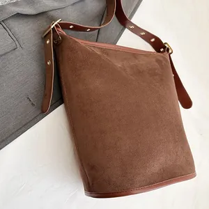 Detail of brown matte suede bucket bag with adjustable leather strap and golden eyelets