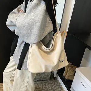 Detail of a large cream-colored hobo shoulder bag with a silver metal plaque and soft leather