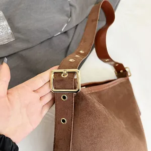 Detail of brown suede bucket bag featuring wide shoulder strap and gold square metal buckle
