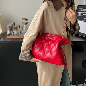Close-up of bright red quilted leather bucket bag with golden chain strap on beige coat