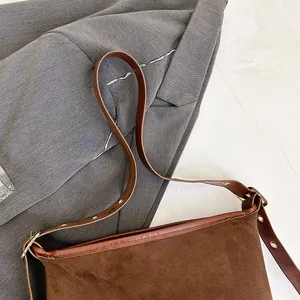 Detail of dark brown suede bucket bag featuring leather trim and metallic buckle accents