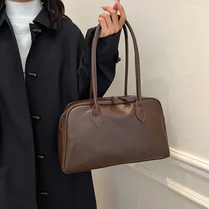Detail of dark brown leather tote bag with long straps worn on shoulder over black coat