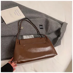 Detail of a brown glossy leather shoulder bag with chain strap on grey coat background