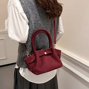 Detail of burgundy suede tote bag featuring a bow accent and adjustable shoulder strap